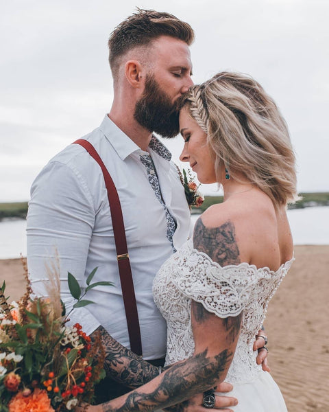 Couple embrace in wedding attire on a beach.
