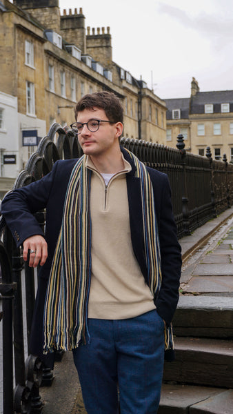 Model wearing a men's winter outfit consisting of a quarter-zip jumper, scarf, jeans, and jacket.