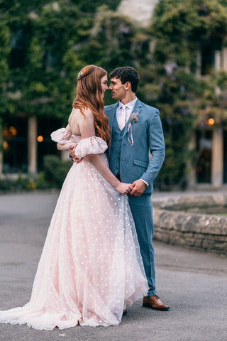 Groom wearing Wells suit stands next to his bride outside venue.