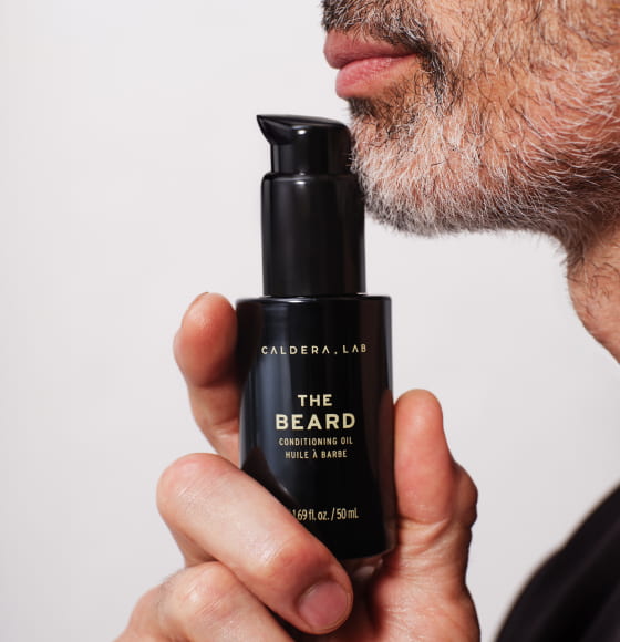 The Beard conditioning oil by Caldera Lab held next to the chin of a man with a short beard
