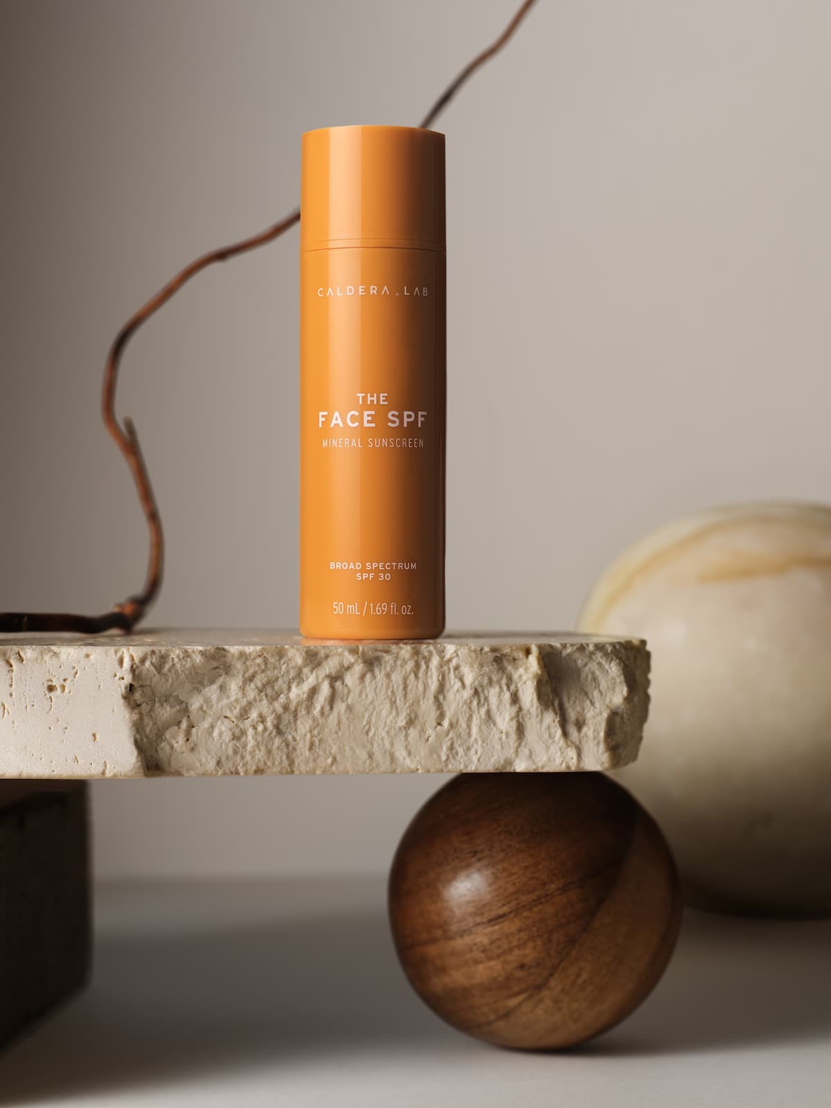 The Face SPF by calderalab in orange packaging placed atop a piece of stone with a brown wooden ball underneath artistically shot.