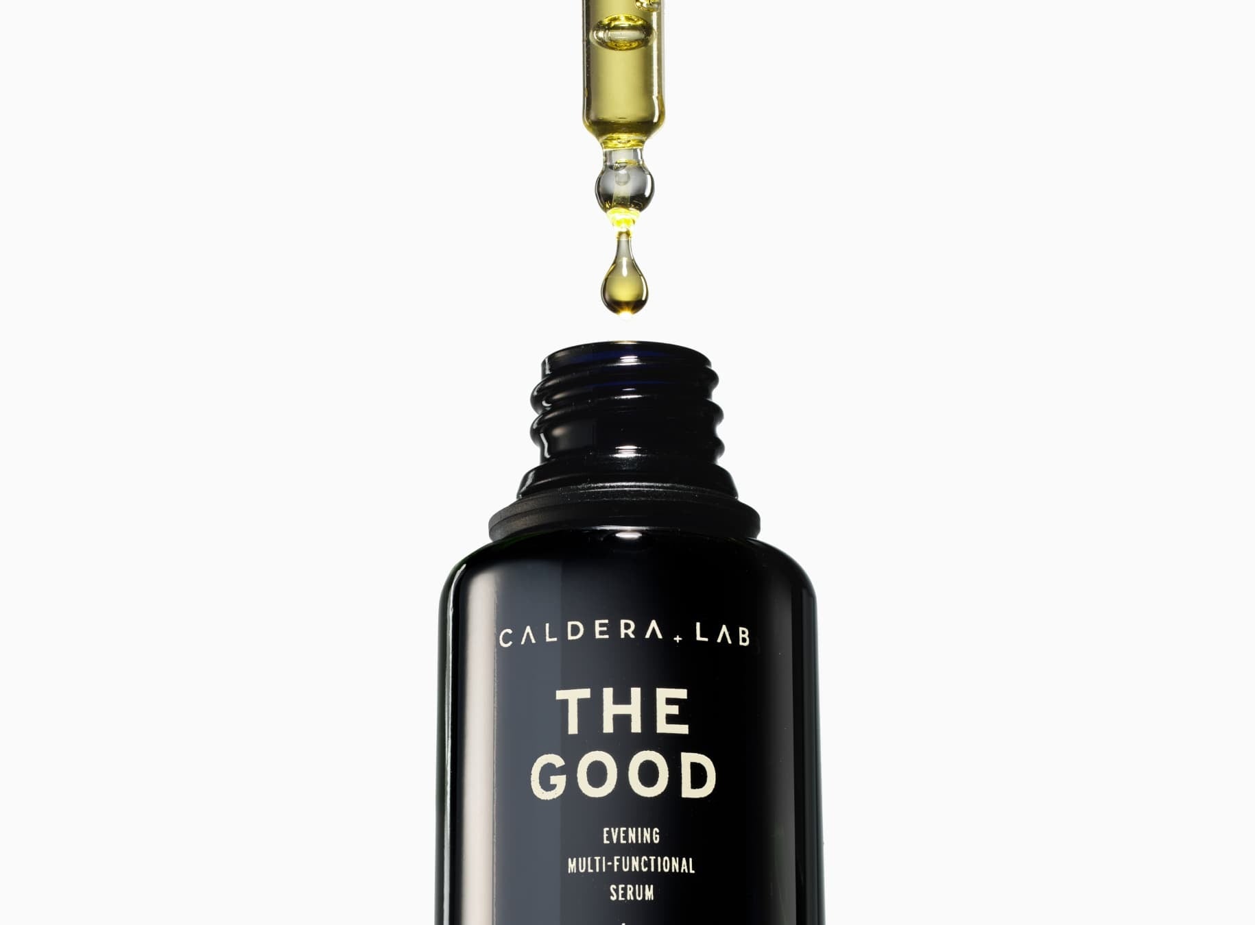 The dropper dispensing a drop of The Good Serum into a black glass bottle.