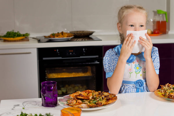 Little blond girl eating a large plate of pizza wiping mouth with napkin