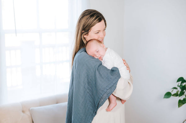 sleeping baby resting on mother's shoulder covered by a muslin swaddle wrap