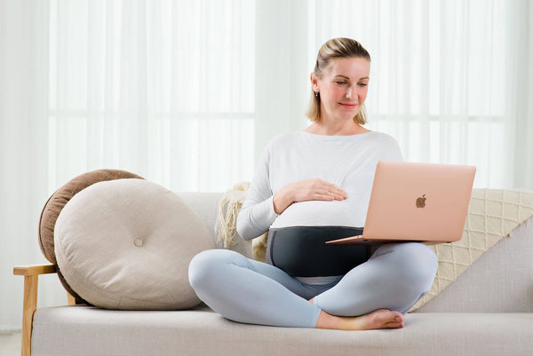 pregnant woman on a couch working on her laptop