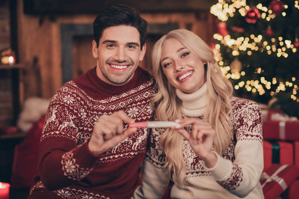 Photo of funky couple hold pregnancy test wear red jumpers indoors near tree on x-mas eve