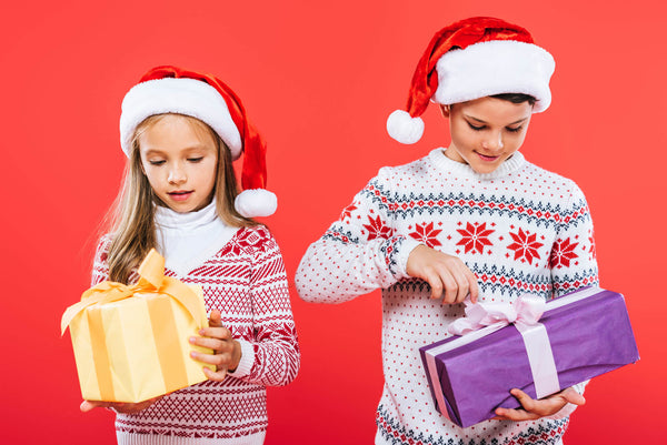 Two Smiling Kids in Santa Hats opening Presents
