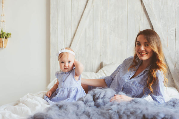 Happy mother and 9 month old baby in matching pajamas playing in bedroom in the morning