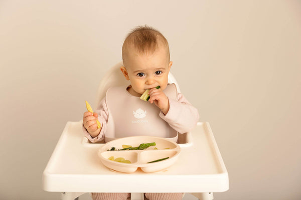 baby eating solid food on a high chair