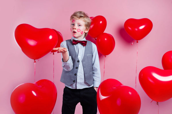 Funny little boy with red kisses on the skin in red balloons in the shape of a heart