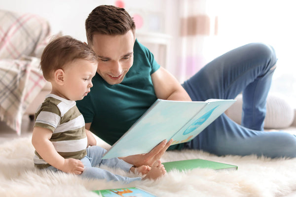 Young father reading book with his cute little son at home