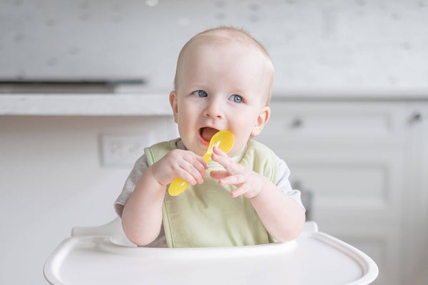 baby chewing on a spoon on a high chair