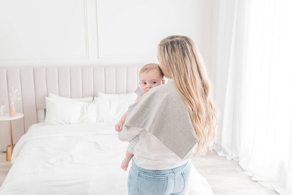 mother carrying a newborn baby resting on shoulder with KeaBabies Lumi Muslin Burp Cloth