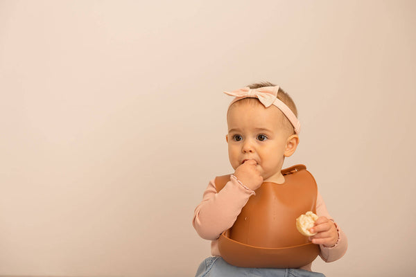 baby girl eating a cookie wearing a silicone bib food catcher