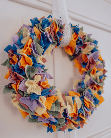 Colorful door wreath made of scraps of fabric DIY in front of a white door