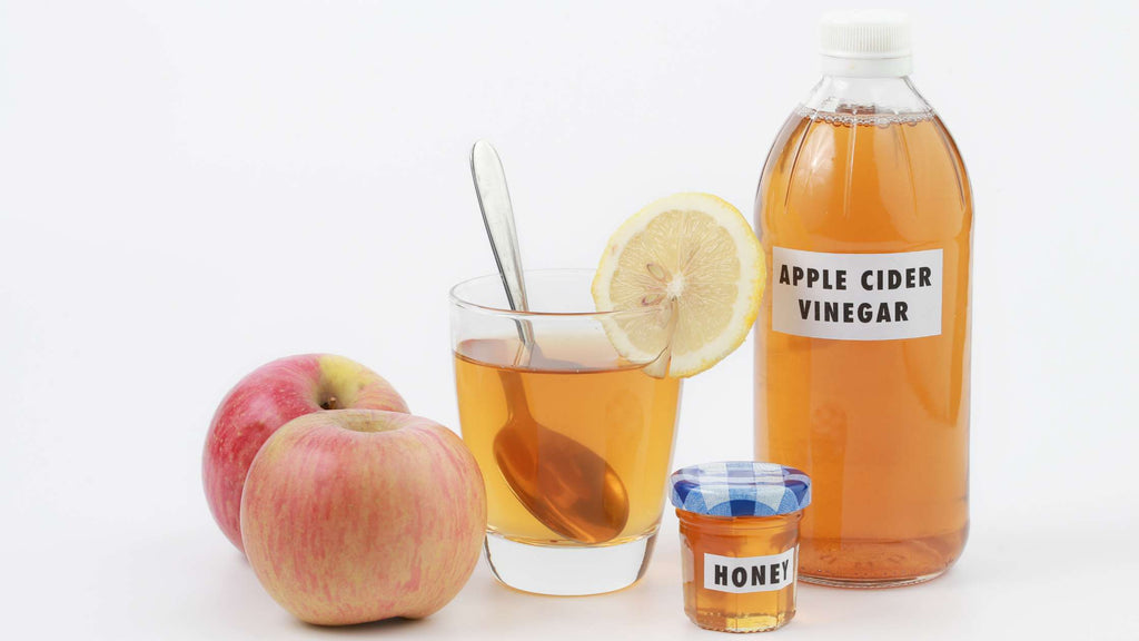 Apple cider vinegar in a glass, honey, apples, and a bottle of apple cider vinegar