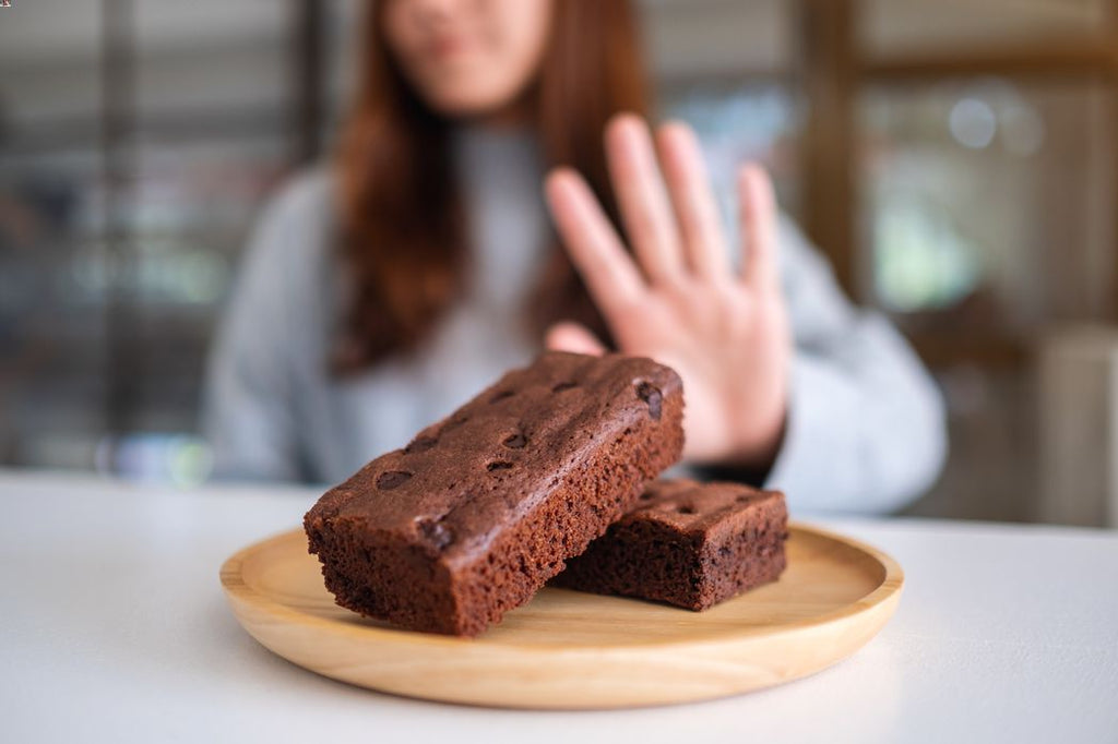 A woman saying no to a plate of brownies. Concept of avoiding junk food, constant snacking, and overeating.