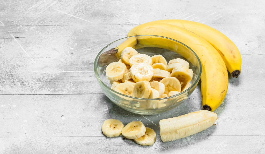 A bowl full of banana slices alongside two whole bananas. 