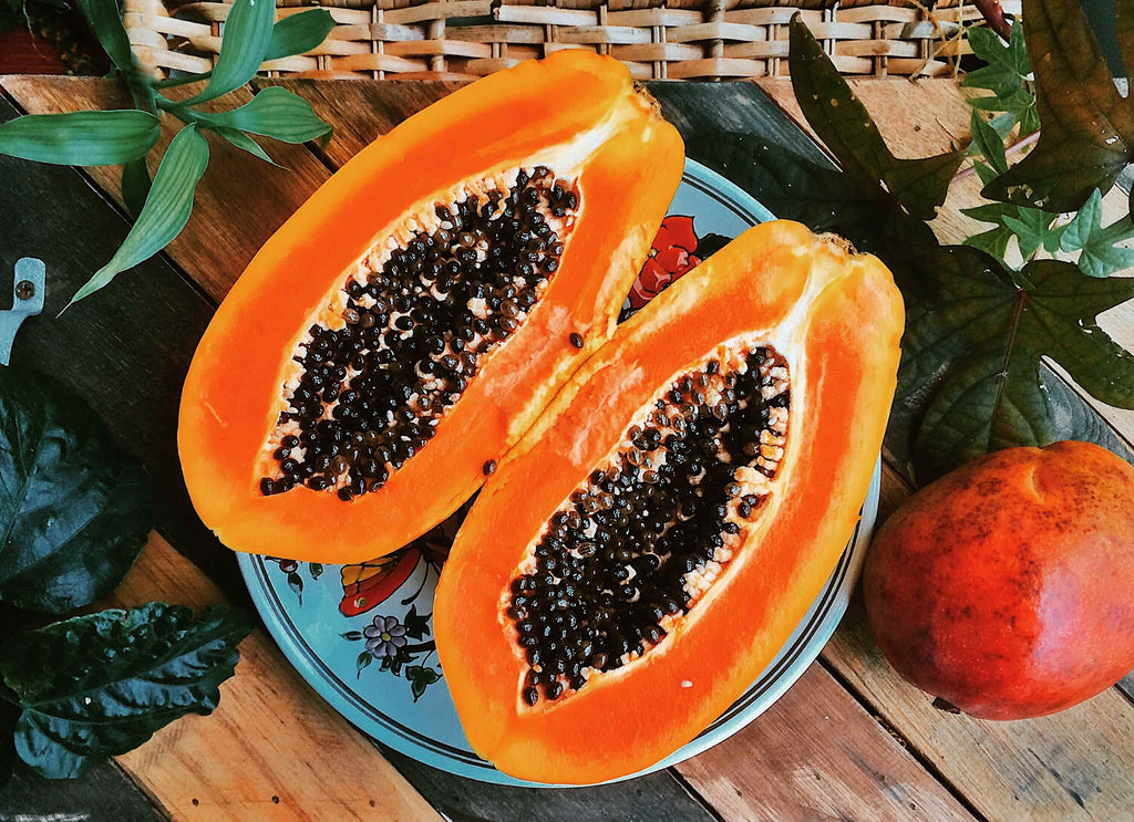 Two slices of a cut papaya on a table full of tropical fruits.