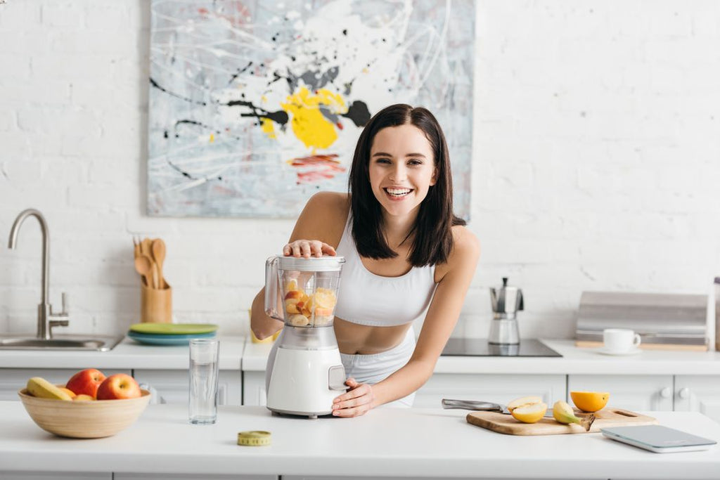 Woman standing in a kitchen making a smoothie, surrounded by low calorie healthy foods.