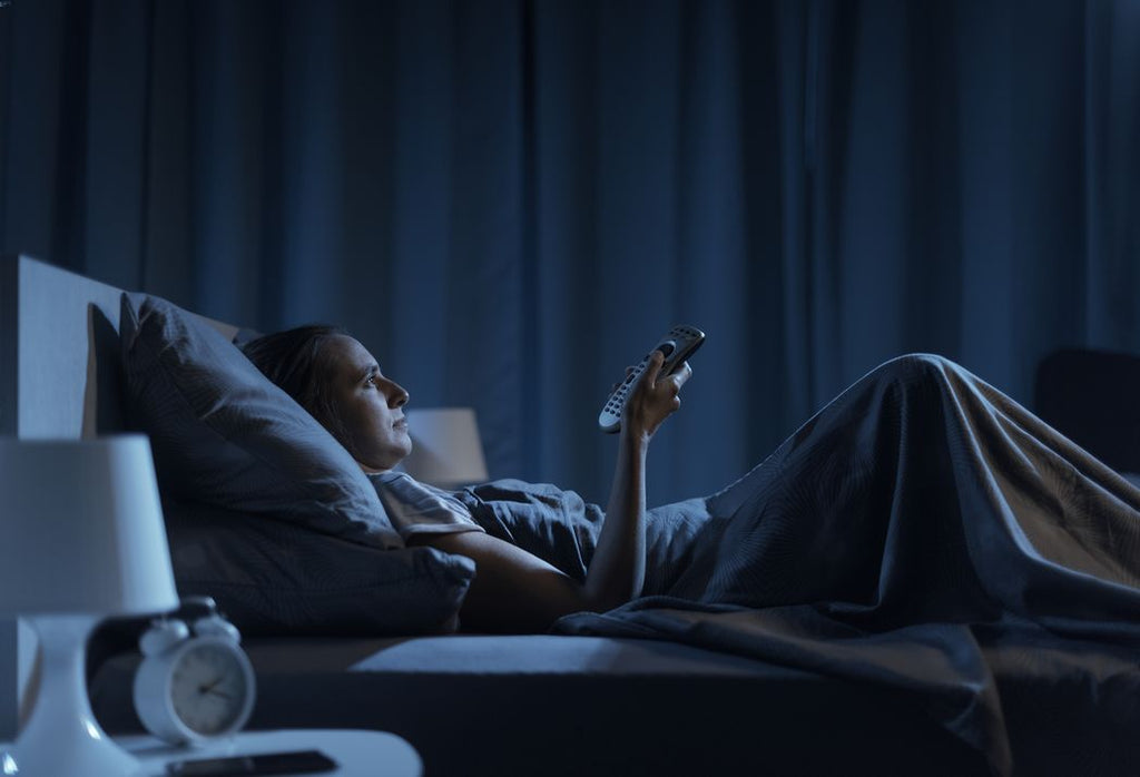 Woman lying awake in bed, watching television, not getting enough sleep.