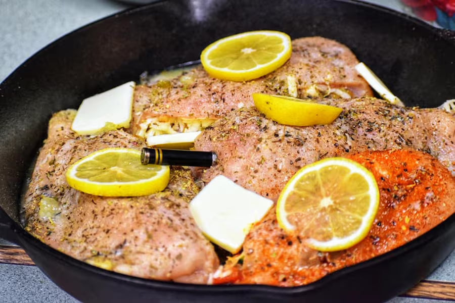 Lemon halves, fresh rosemary, and garlic cloves on a wooden board, ready for a marinade.
