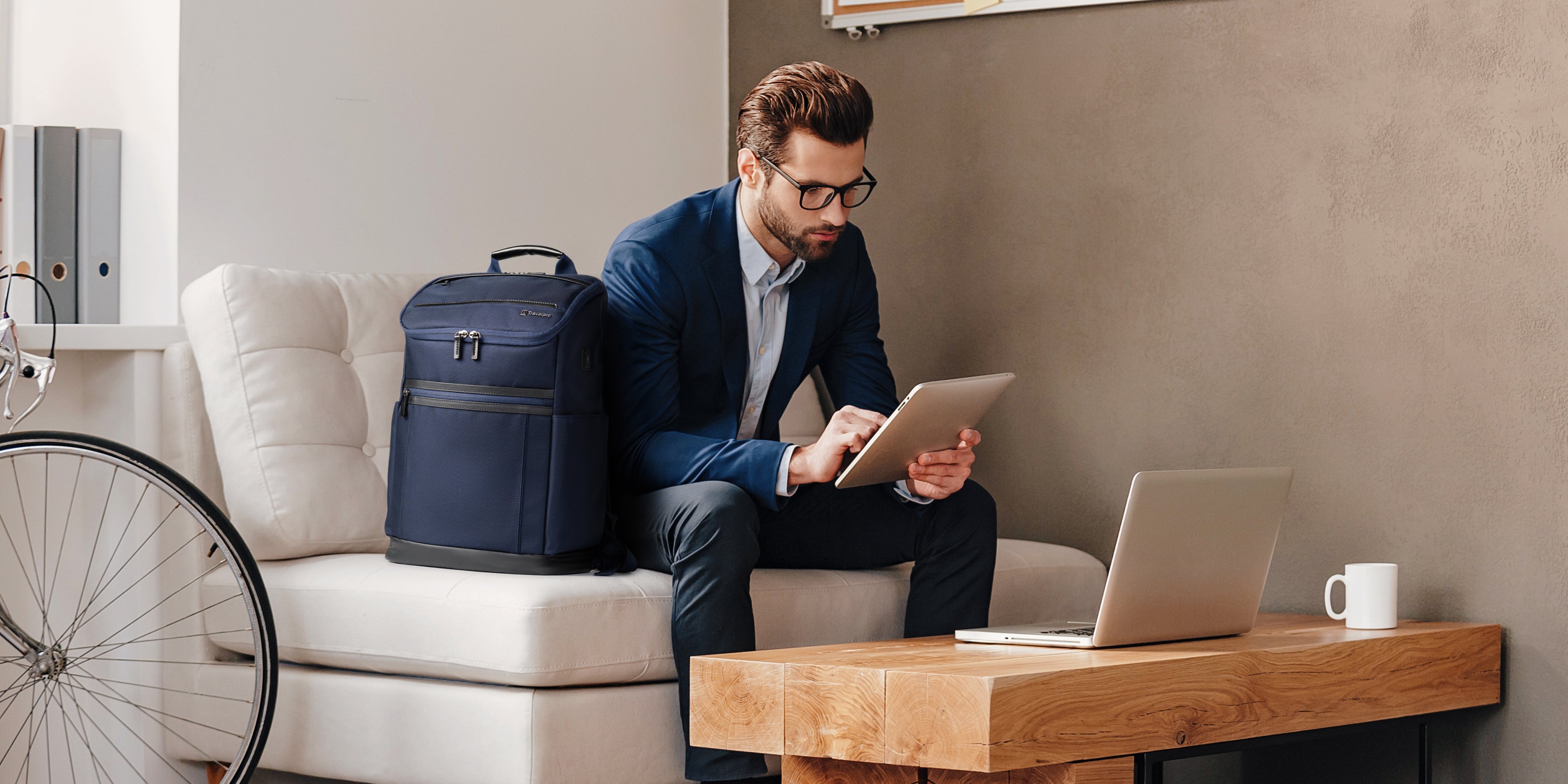 Man sitting on a couch working on laptop with backpack next to him 