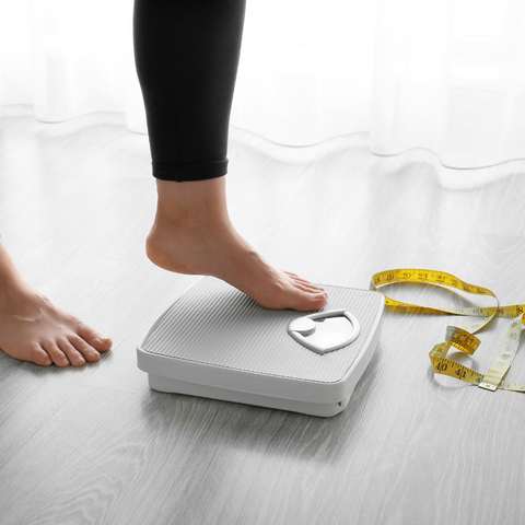 feet of someone stepping on a scale with a measuring tape on the ground