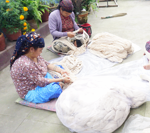 Production Process: Around 500 KG of white yarn in a plastic bag. 2 Nepalese women shifting through the yarn.