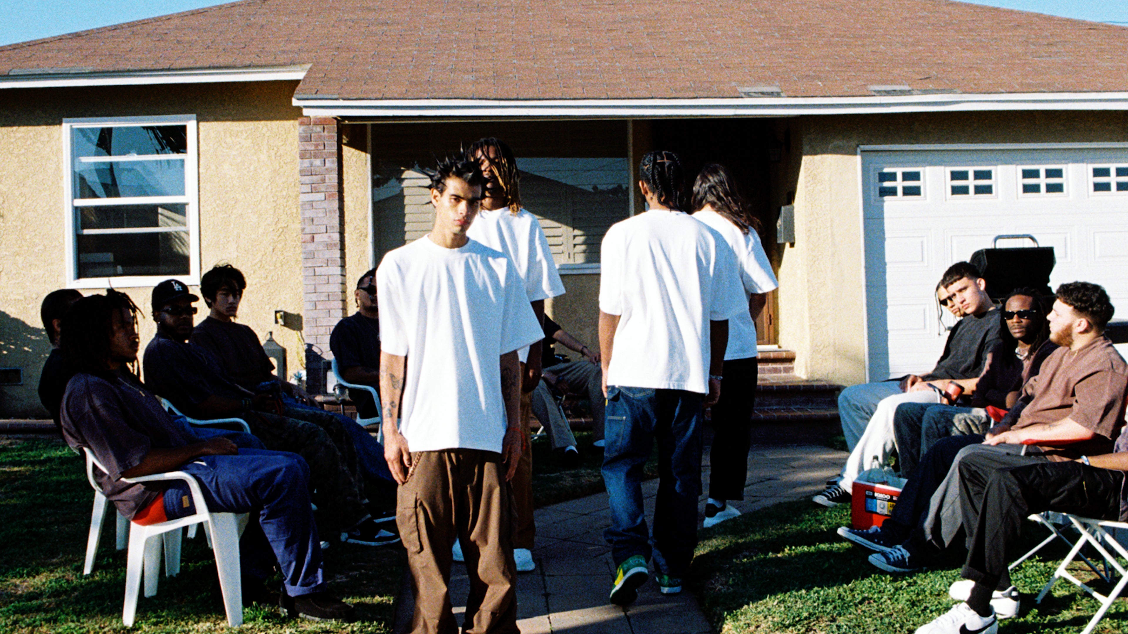 a group of men modeling Shaka Wear Desinger T Shirt on a fashion runway in front of a south central home.
