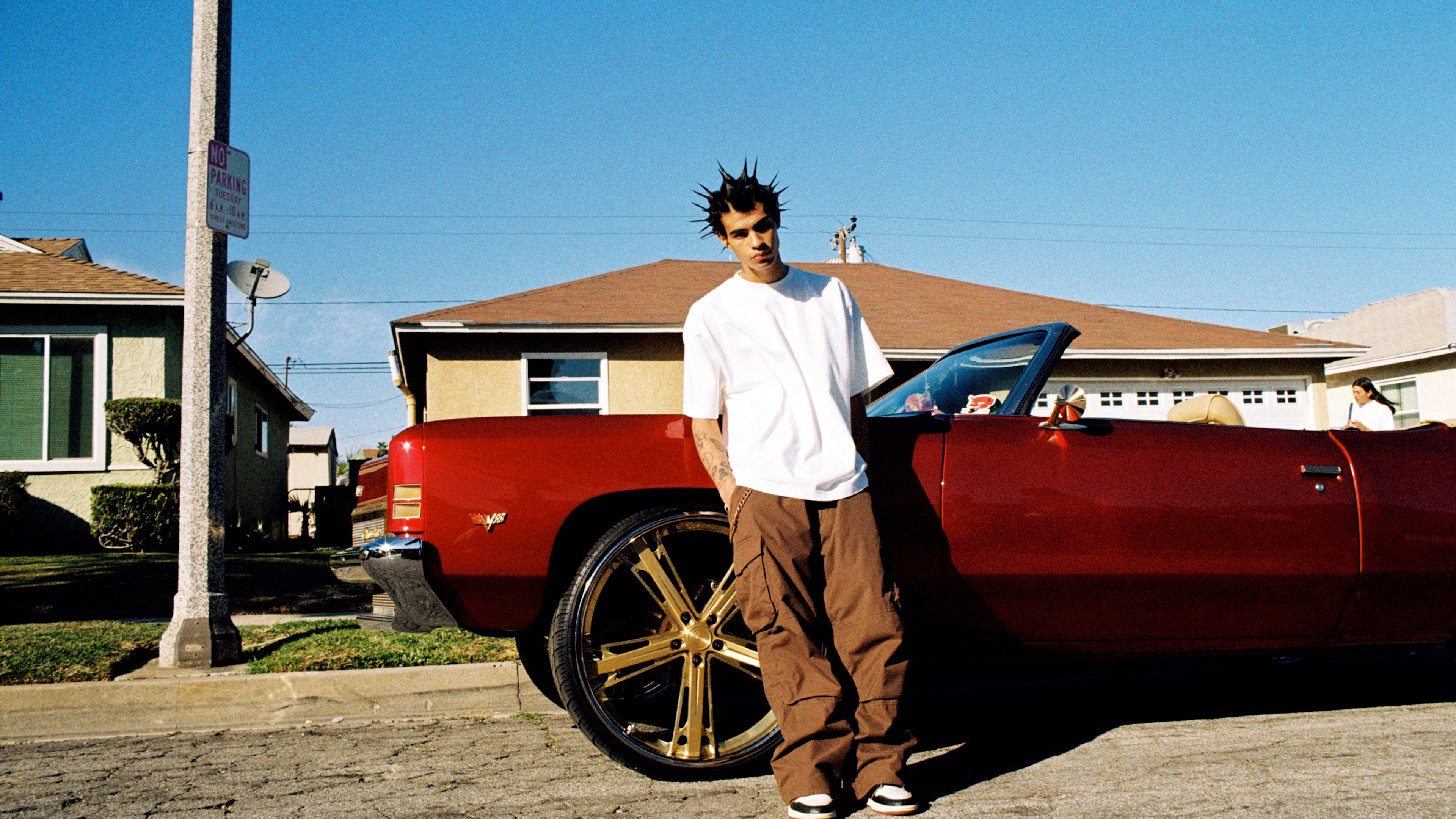 A model wearing Shaka Wear The Designer T shirt standing in front of a lowrider in south central 