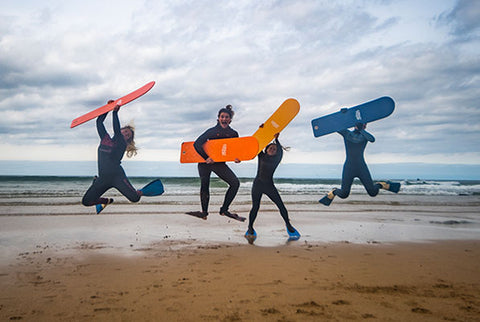 Four people jumping in the air, holding bellyboards on the beach