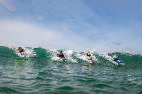 Four people bellyboarding on a wave