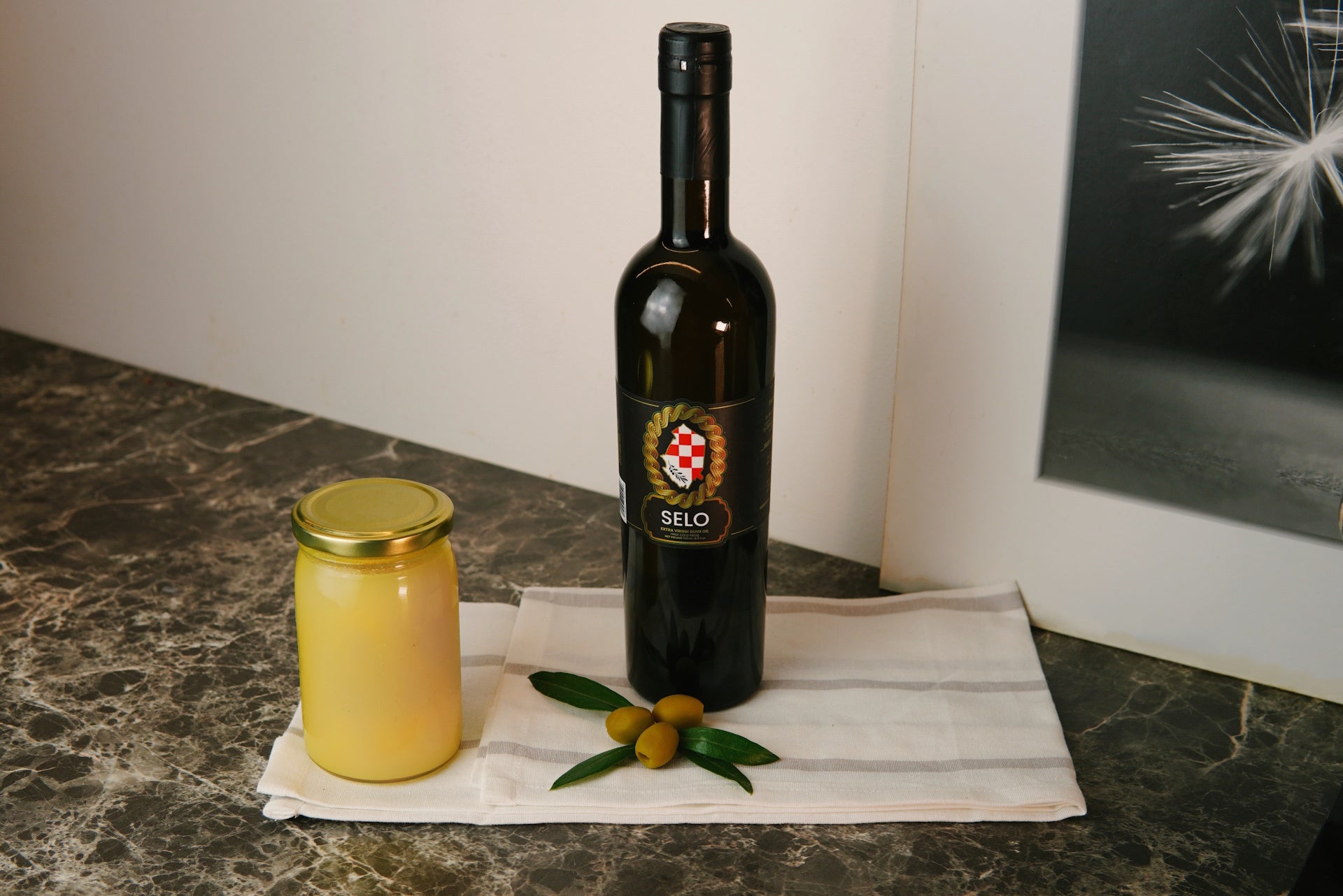 Elegant black bottle of Croatian olive oil next to a container of smooth beef tallow, displayed on a marble surface with fresh olive branches for decoration.