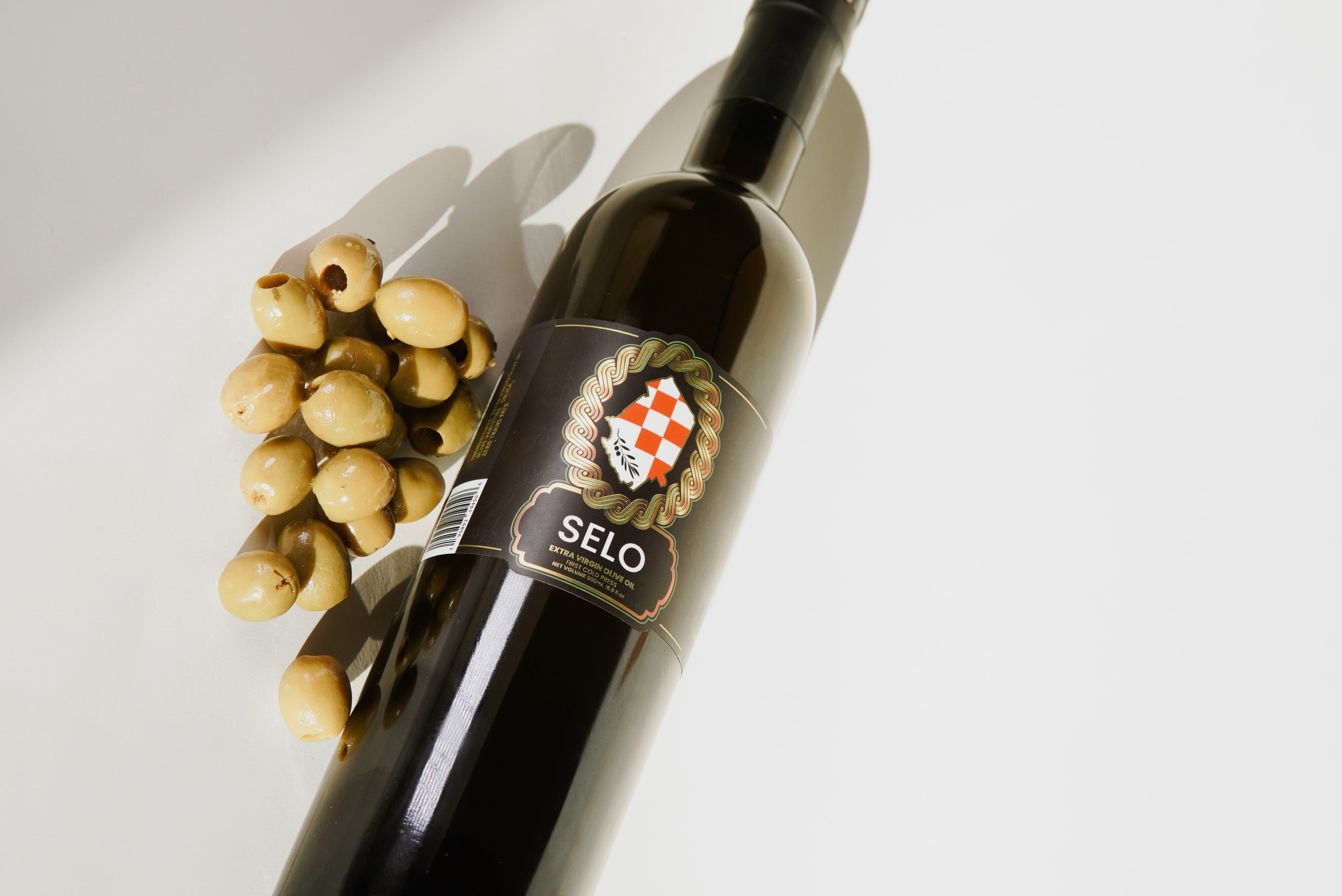A bottle of Selo Croatian Olive Oil showcasing its rich golden hue, featuring the brand name and logo prominently on the label, with a lush green olive branch and olives in the background, representing the high-quality and authentic Croatian olive oil.