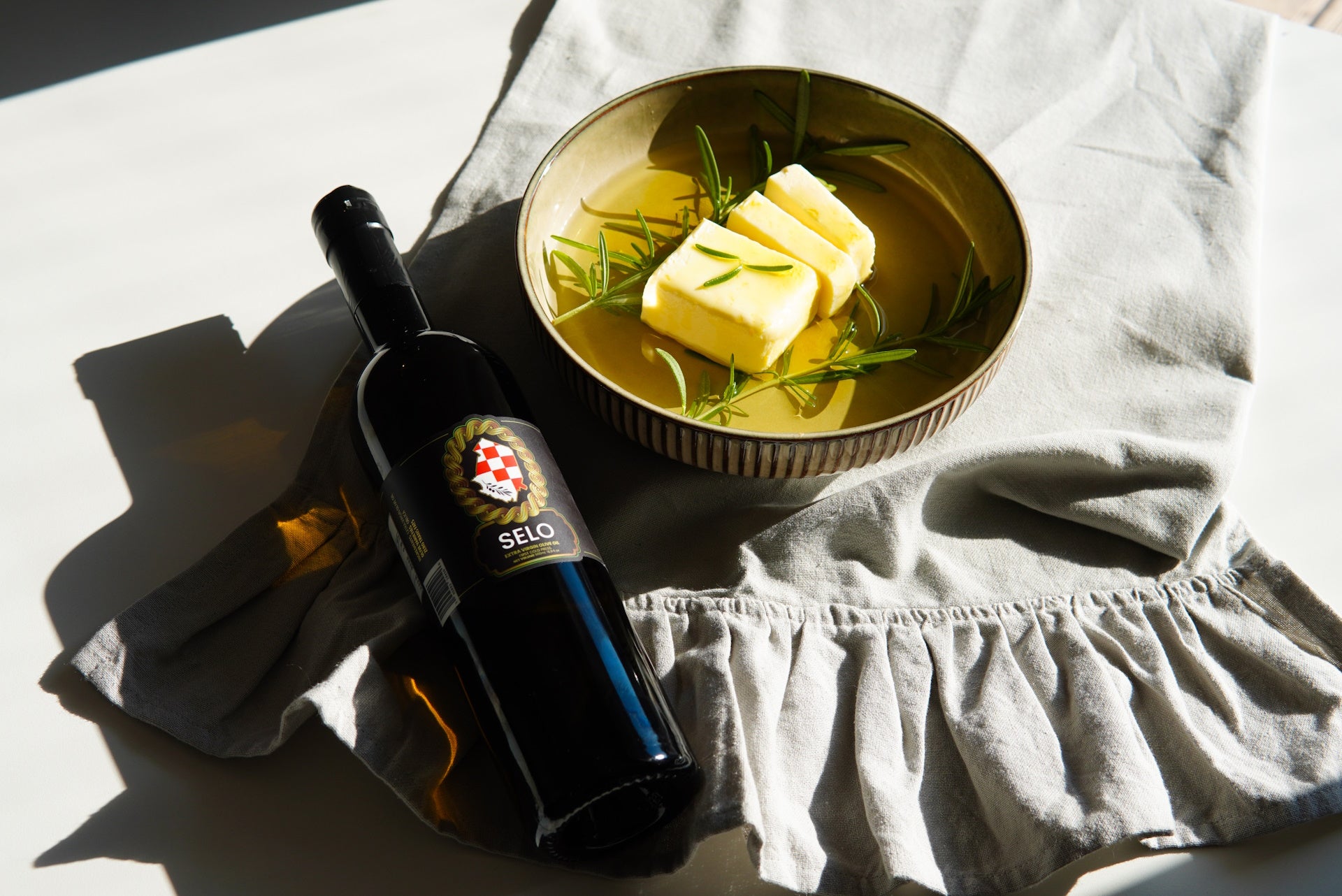 Goat butter melting in a pan, infused with olive oil and fresh rosemary, next to a bottle of Selo Croatian olive oil.