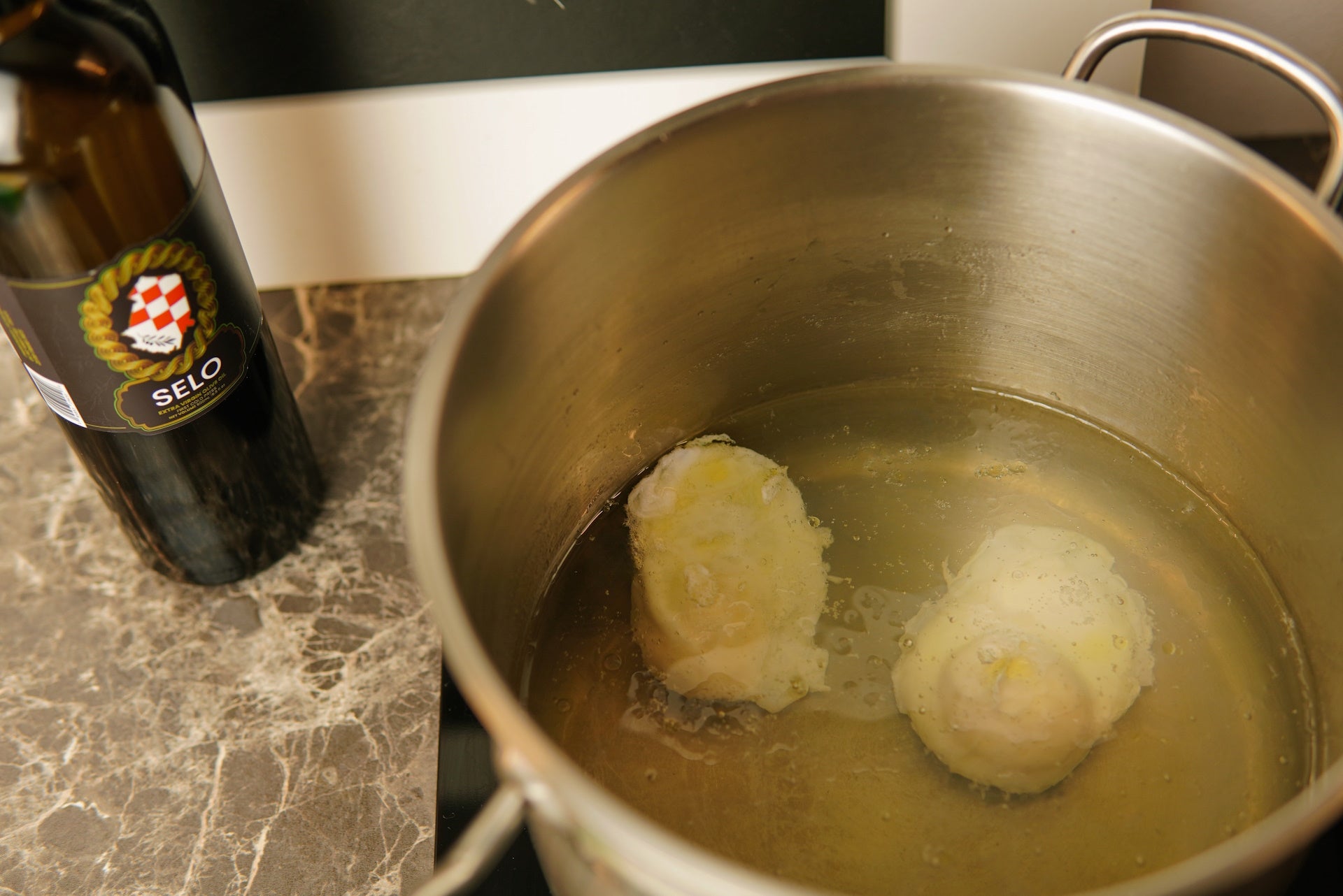 Eggs gently poaching in a pot of simmering water with a swirl of Croatian olive oil on top.