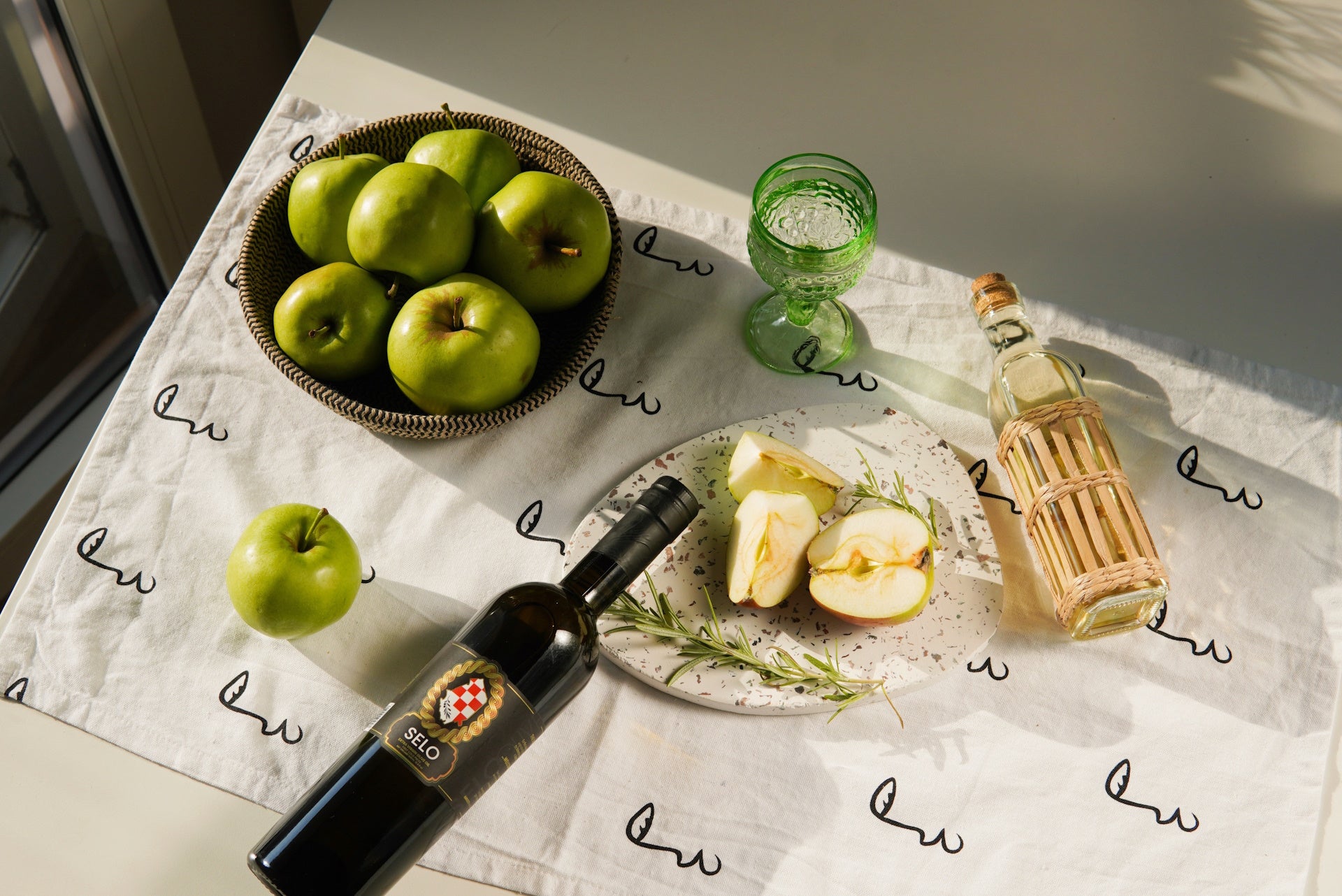 Fresh apples in a bowl alongside another filled with olives, accompanied by a bottle of Croatian olive oil.