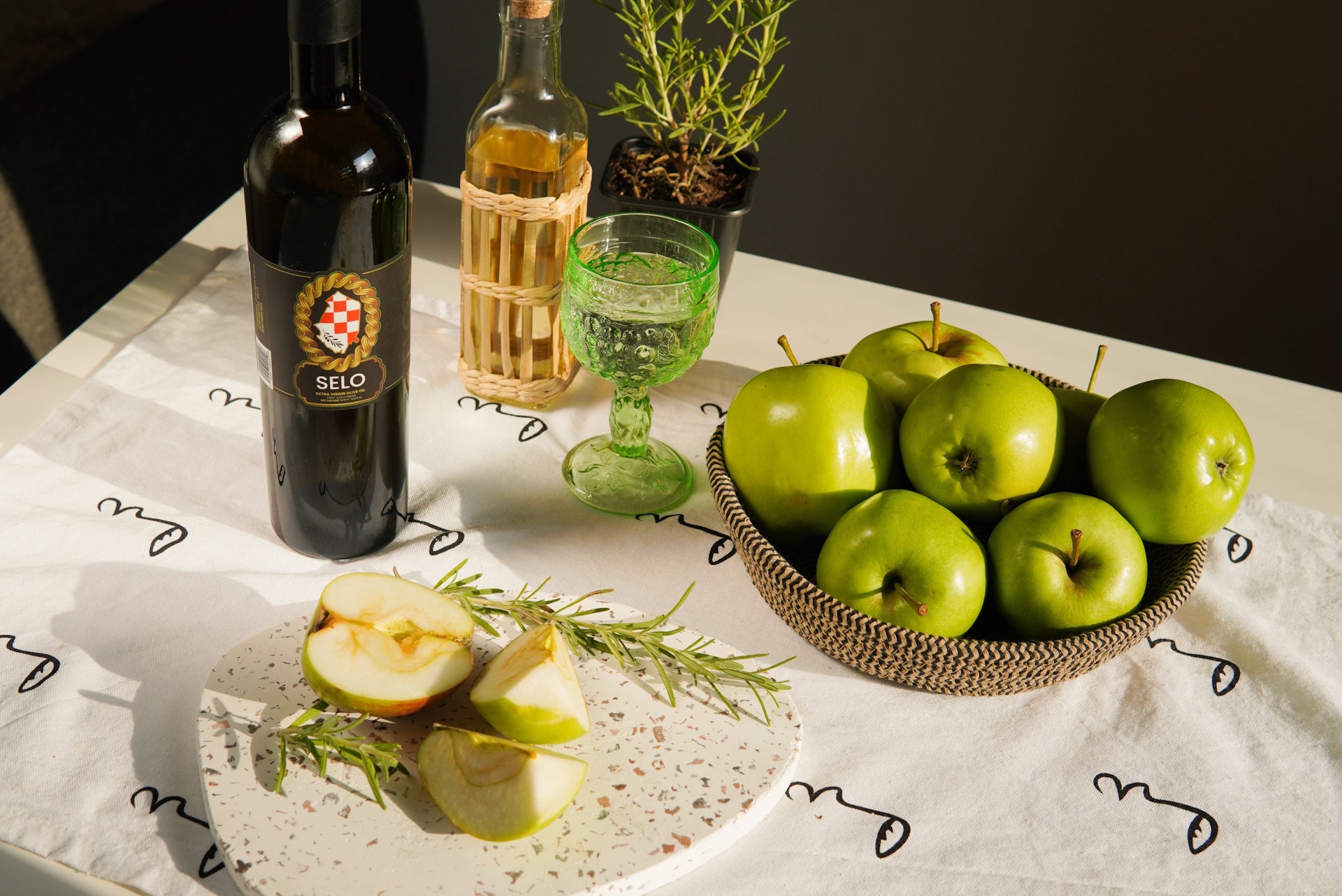 A display of crisp apples in one bowl, olives in another, and a distinct bottle of Croatian olive oil beside them.