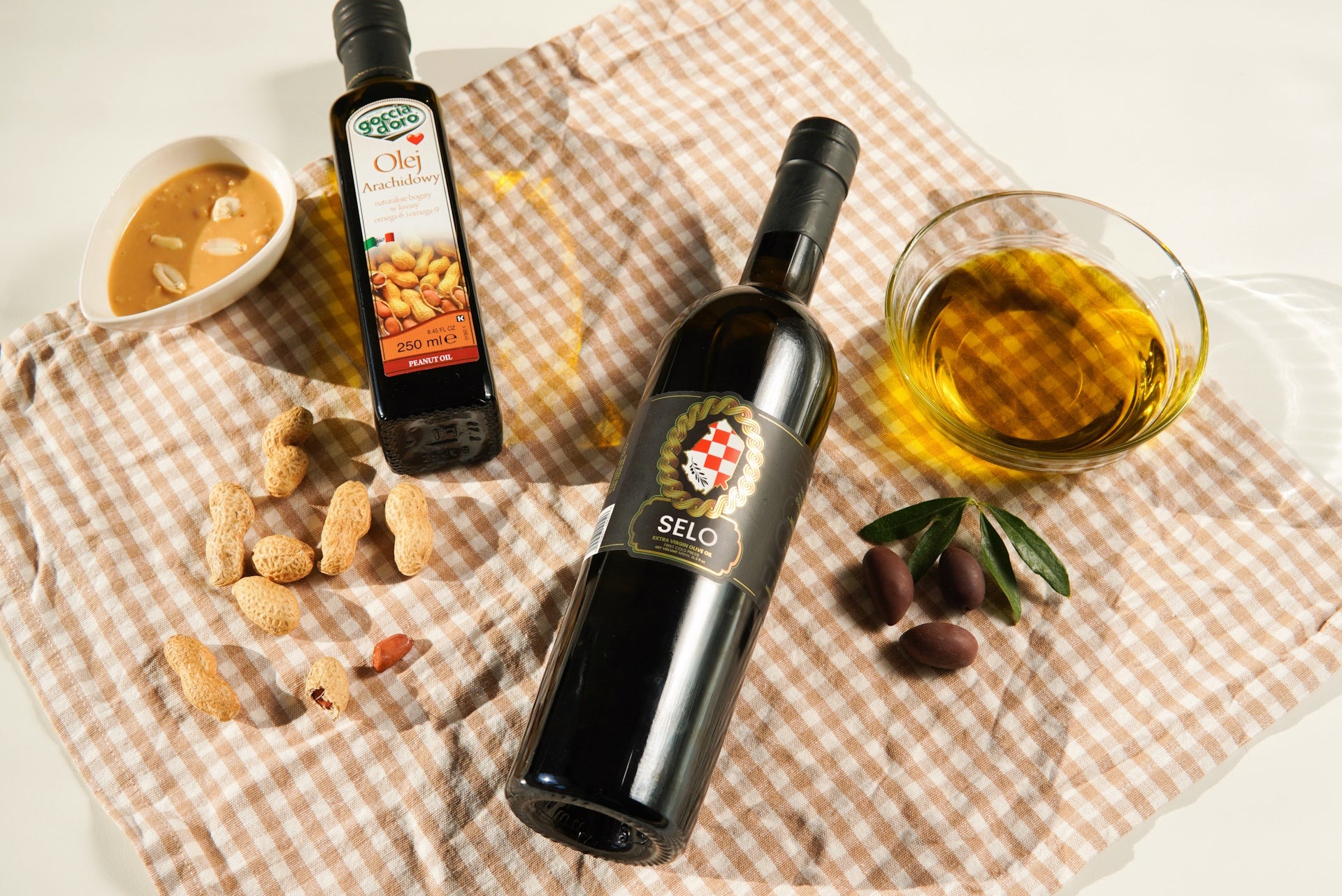 Side-by-side display of a peanut oil bottle and a Croatian olive oil bottle on a kitchen table.