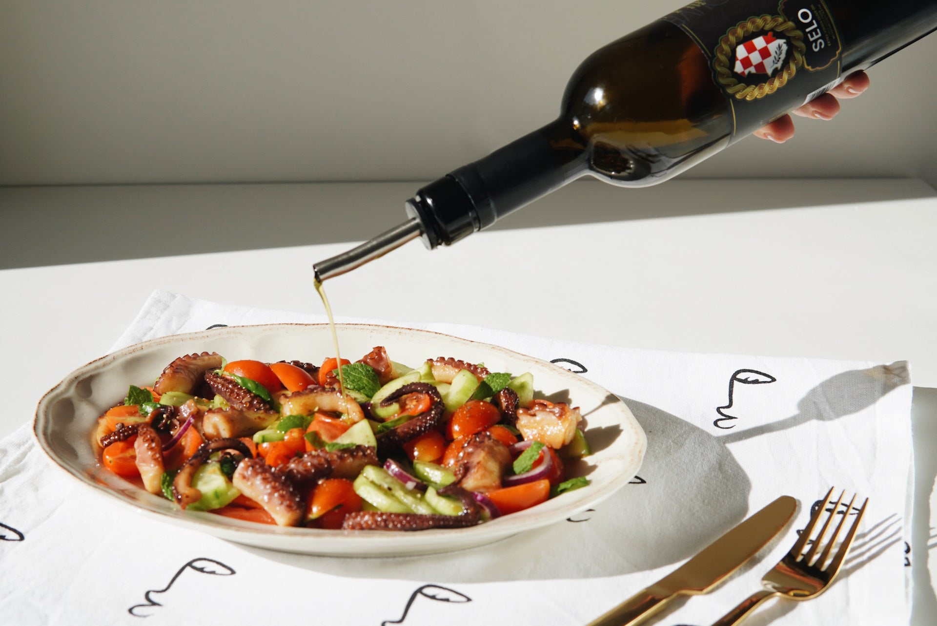 Selo Olive oil being gracefully poured over a delightful octopus and vegetable salad, enhancing its flavors with a golden stream of liquid goodness, creating a visually enticing and appetizing culinary masterpiece.