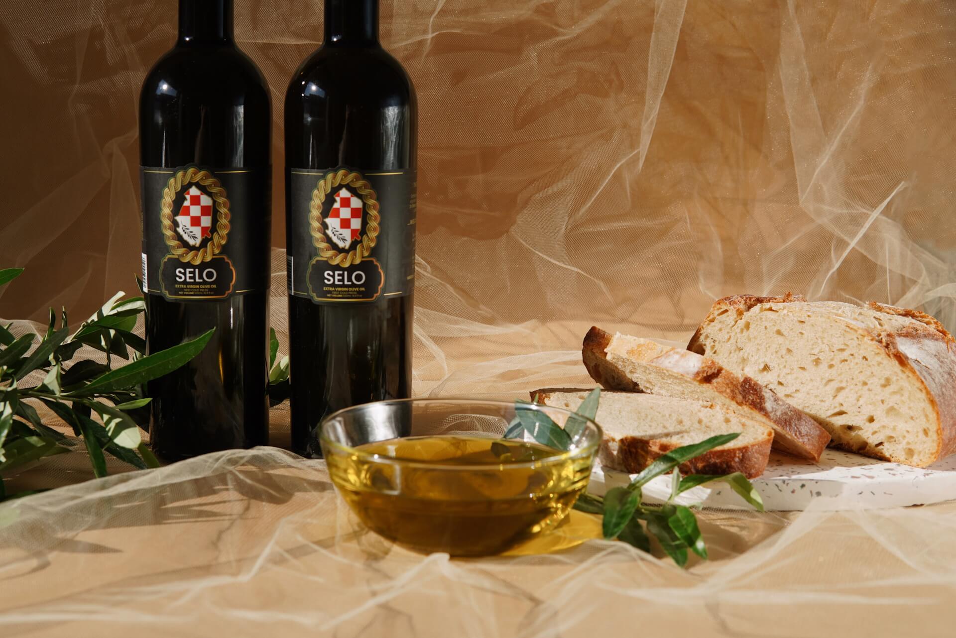 A bottle of Selo Croatian Olive Oil showcasing its rich golden hue, featuring the brand name and logo prominently on the label, with a lush green olive branch and olives in the background, representing the high-quality and authentic Croatian olive oil.