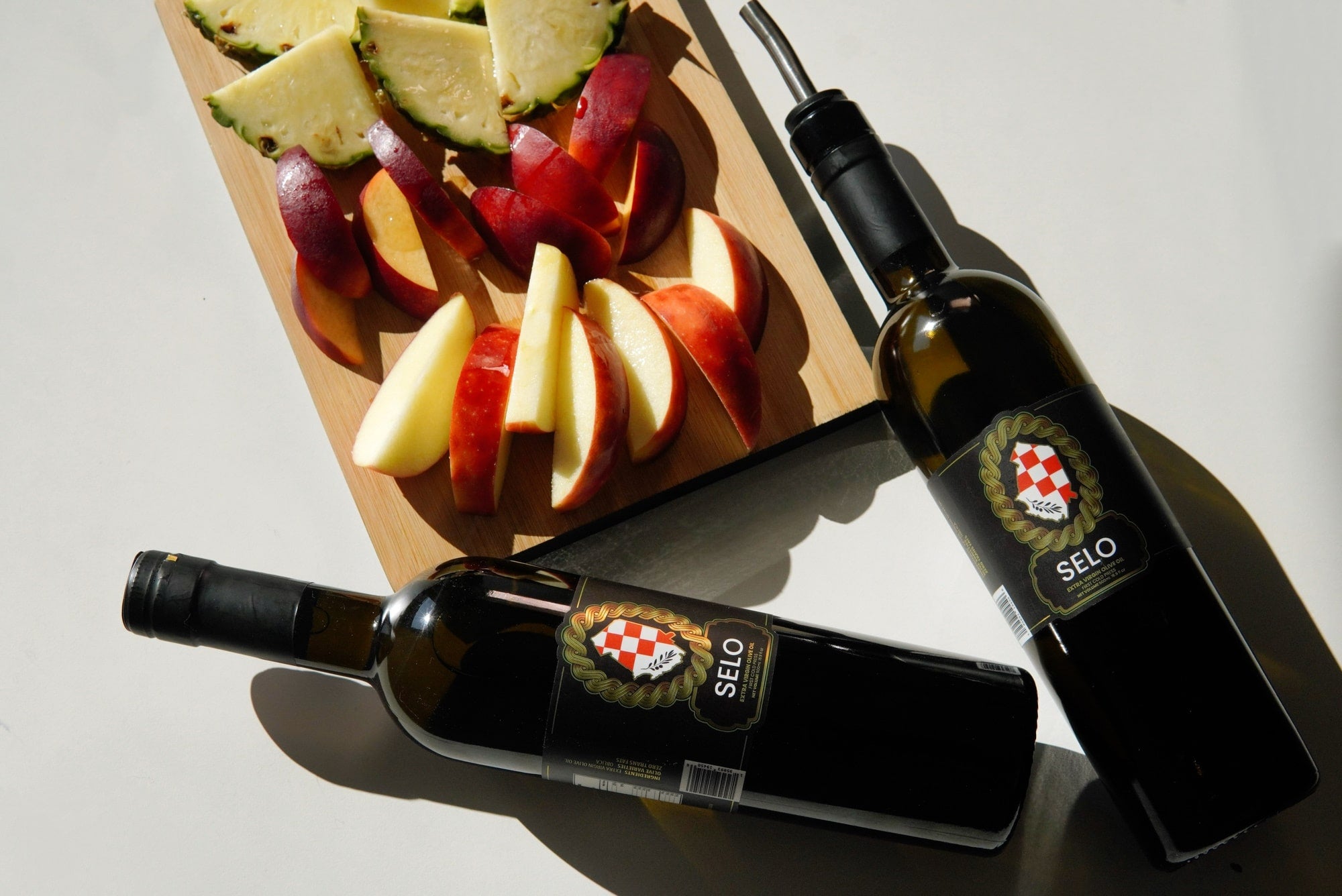 A bottle of Selo Croatian Extra Virgin Olive Oil pouring over juicy red apple slices, highlighting the apples' vibrant color and the oil's rich golden hue.