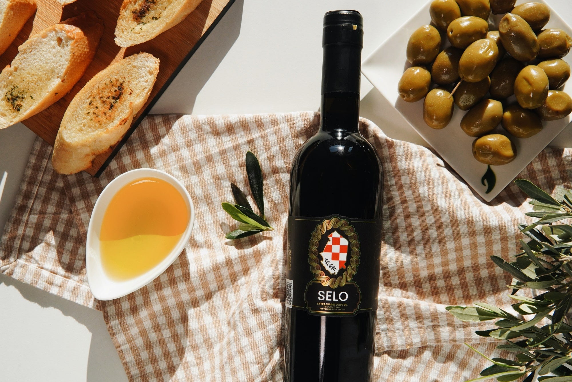 A bottle of Selo Croatian Olive Oil showcasing its rich golden hue, featuring the brand name and logo prominently on the label, with a lush green olive branch and olives in the background, representing the high-quality and authentic Croatian olive oil.'