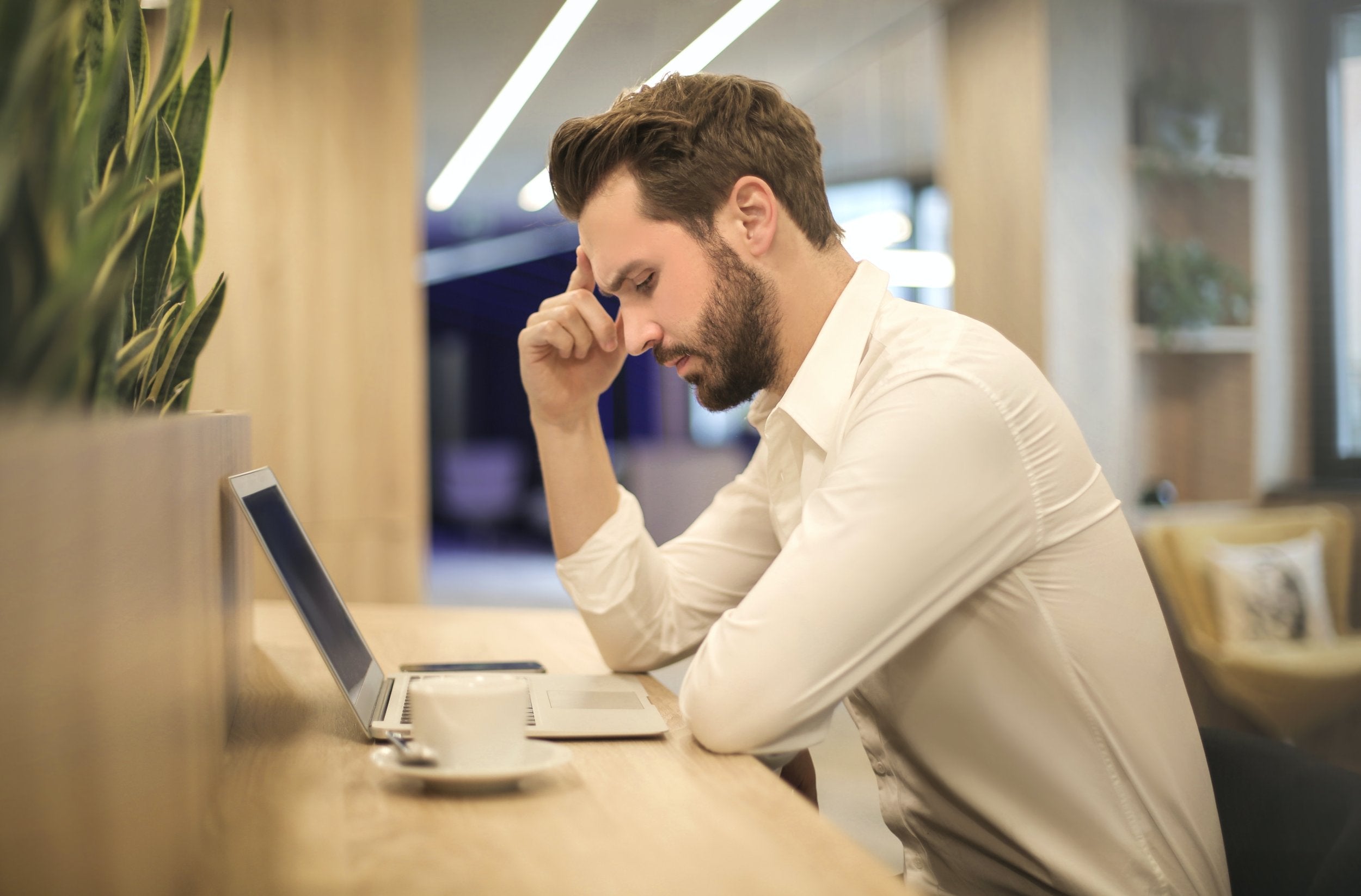 Stressed male in a library with a white shirt and a laptop and coffee