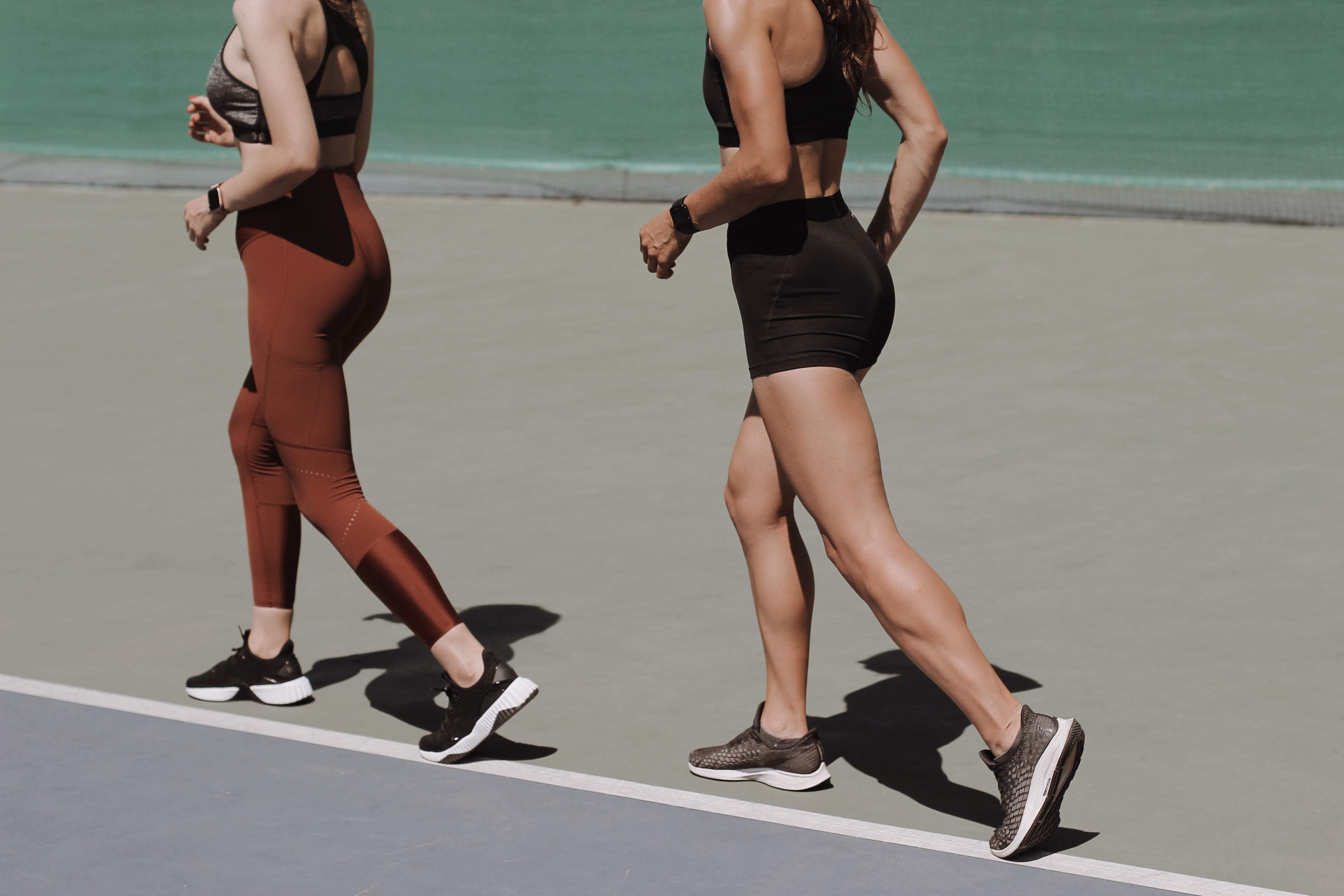two women running on a tennis court in the summer showing their legs