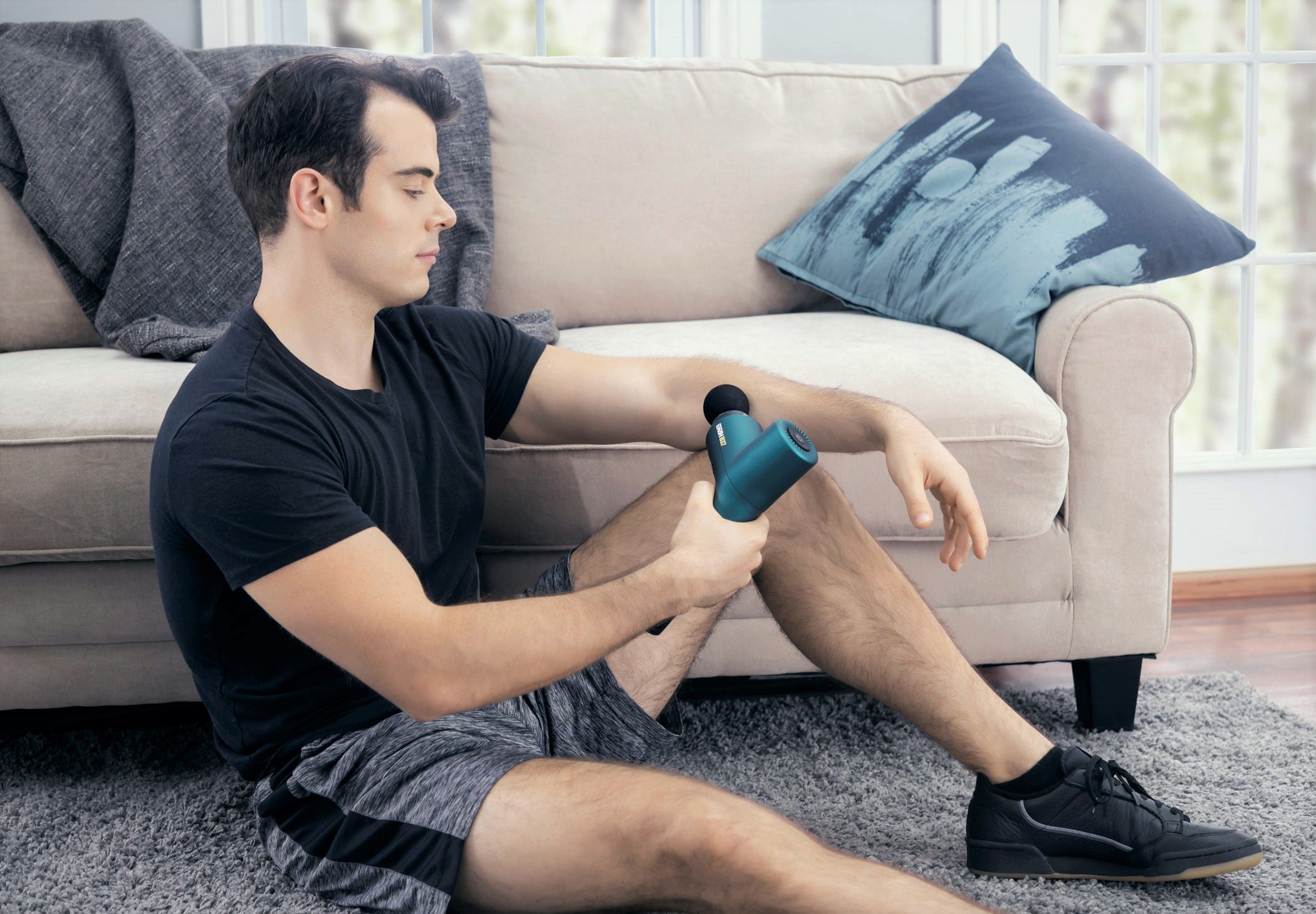 Young man in black t-shirt using a massage gun in a living room