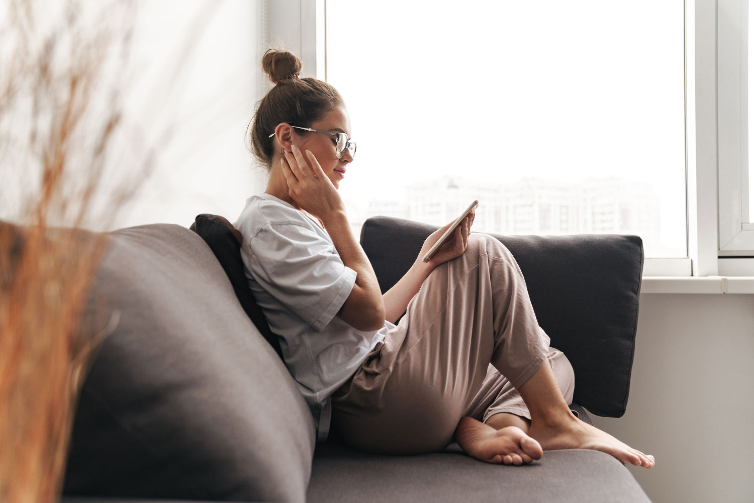 concentrated nice woman in eyeglasses using cellphone while sitting on sofa at living room