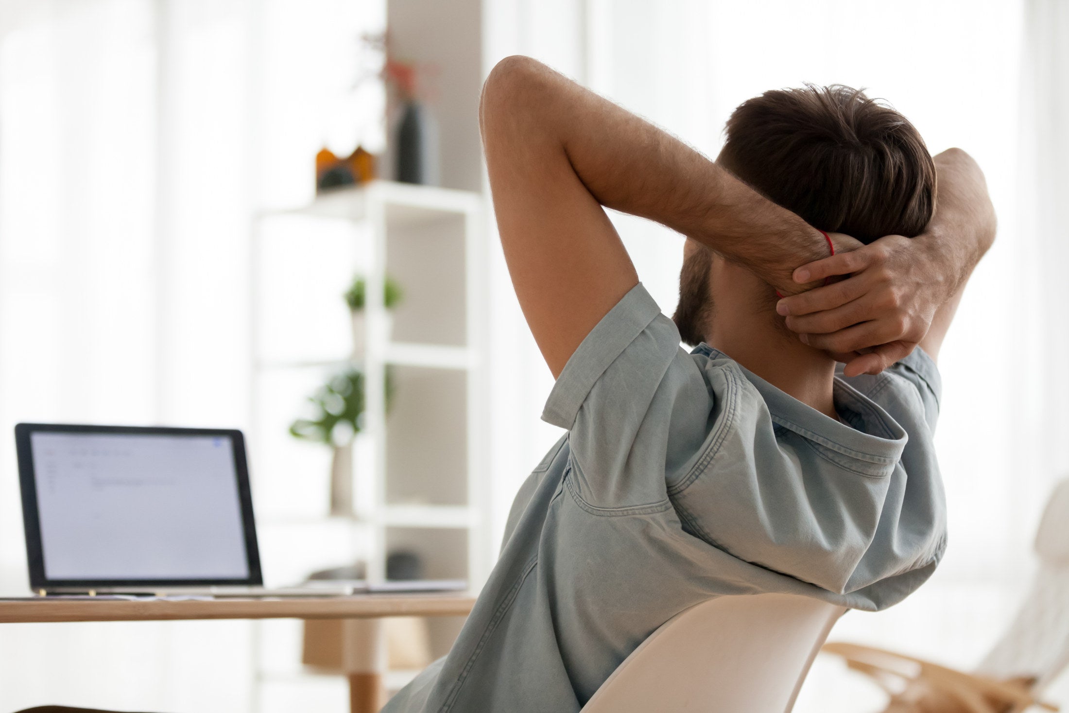 Rear back view at relaxed healthy man taking break for rest finished work sitting at desk stretching with hands behind head enjoying peaceful mood lounge relaxation feeling stress relief at workplace