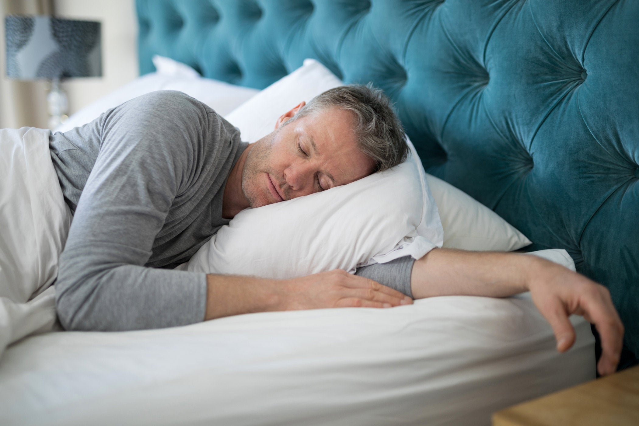 Man sleeping peacefully on a king sized bed with a blue tufted headboard